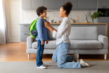 Mother adjusting son's backpack before school in living room