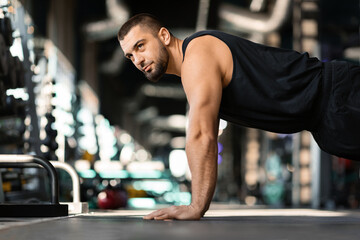 Motivated young male doing floor push-ups exercises while training in gym