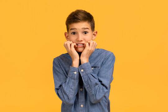 Anxious teenage boy in denim shirt biting nails and looking at camera