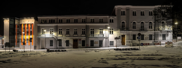 Zabytkowe budynki ratusza, oświetlone nocą, wśród puszystego śniegu. Pięknie wyglądający ratusz z ozdobnie podświetloną fasadą nocą, w śnieżnej aurze.