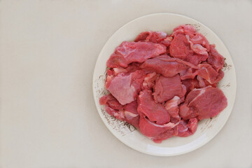 Meat on a ceramic dish on beige background. Raw beef for cooking. Top view.