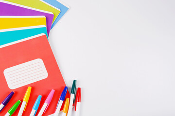 A stack of colorful school notebooks lies in a fan, and pens with colorful caps are highlighted on a white background.Purchase, sale of school supplies, stationery store.Copyspace