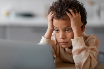 Homeschooling Difficulties. Upset Black Boy Using Laptop At Home And Touching Head