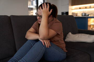 Obraz premium Thoughtful down syndrome woman sitting in living room and looking away