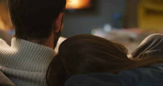 Couple, holding hands and cuddle by fireplace, relax in living room in winter and bonding with love and care at home. Cozy, snuggling or hug, back of people on couch with time together and security