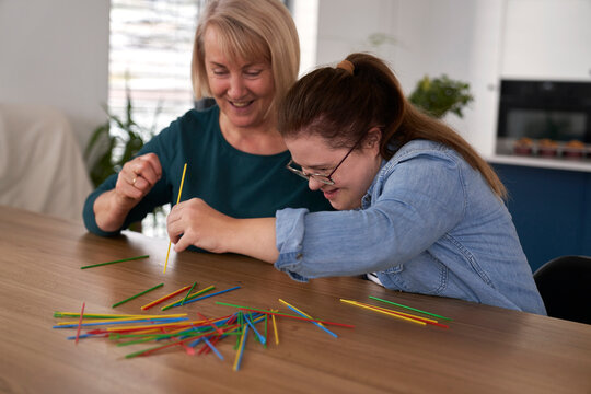 Down syndrome woman and her mother playing pick up sticks at home