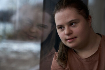 Thoughtful down syndrome woman sitting next to window and looking away