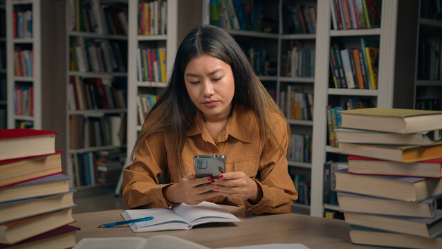 Asian girl student sitting in library write doing homework frustrated young woman getting notification on mobile phone reading bad news failing exam dropout from college losing scholarship feel upset