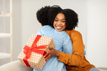 A woman with a beaming smile gives a warm hug to a person while holding a heart-patterned gift box