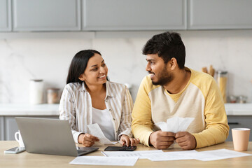 Smiling indian couple with laptop in kitchen calculating bills