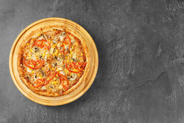 Homemade Italian pizza with melted mozzarella cheese mushrooms, corn and tomato on round wooden dish on gray concrete background. Banner, header with copy space