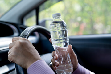 Asian woman driver holding bottle for drink water while driving a car. Plastic hot water bottle...