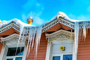 Icicles in winter and spring in a selective focus. Roof of the house is covered with snow and ice. Icicles hang from the roof, melting on a bright sunny day. Danger, the falling icicles. Thaw.