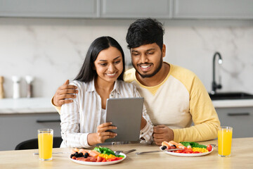 Loving Indian Couple Eating Breakfast Together And Using Digital Tablet