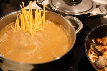 Pasta cooking in boiling water beside seafood stew.