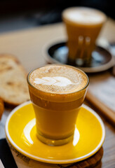 Artisan latte in yellow cup with saucer.