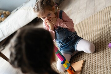 Two little 6s 7s sisters pretty daughters spend free playtime seated on carpet warm floor in modern...