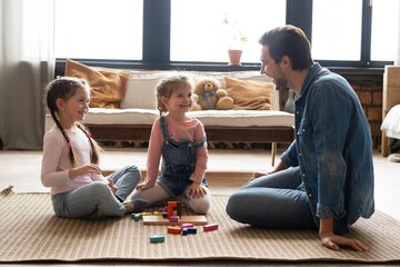 Caucasian family with their little daughters builds tower while playing on floor of children's...