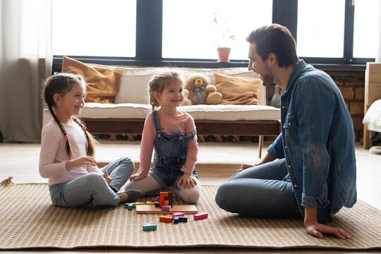 Caucasian family with their little daughters builds tower while playing on floor of children's room. Dad and two girls have fun together