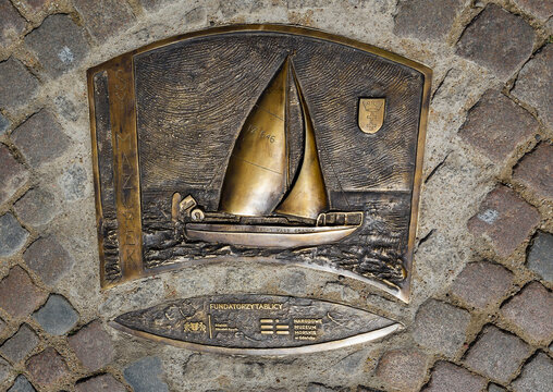 Gdansk, Poland - July 15, 2023: Copper plate with an image of a sailing boat  on the road in the port of Gdansk. Polish text - Founders of the administration.
