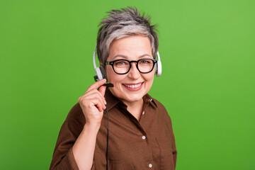 Portrait of positive person with gray hairstyle wear headset touch microphone speak with client isolated on green color background