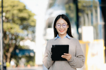 Confident Asian woman with a smile standing holding notepad and tablet at out side office. big city .