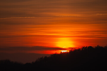 Orange solar disk seen above the forest. Wonderful sunset at the end of day