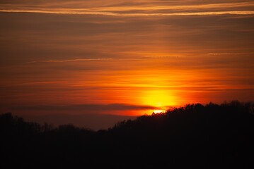 Orange solar disk seen above the forest. Wonderful sunset at the end of day