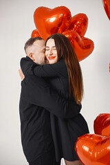 Man and woman holding bunch of heart-shaped red ballons and posing in studio