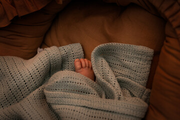 A baby's foot covered with a blanket in warm lighting. The concept of health and warmth in rooms where children stay especially in winter.