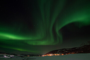 Spectacular northern lights (Aurora Borealis) dancing over a snowy landscape near Tromsø, Norway.