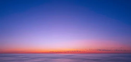 Poster Idyllic natural sunrise sky background over sea in the early morning with motion blur of flowing water surface in panoramic view, beautiful tranquil seascape view in sunset time  © Prapat
