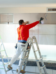 Plasterboard worker installs a plasterboard wall on the kitchen cabinets to cover the extractor pipe of the hood. - 724762703