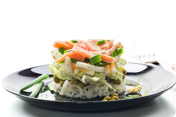 Layered salad of cabbage and other vegetables with pieces of red fish in a plate.