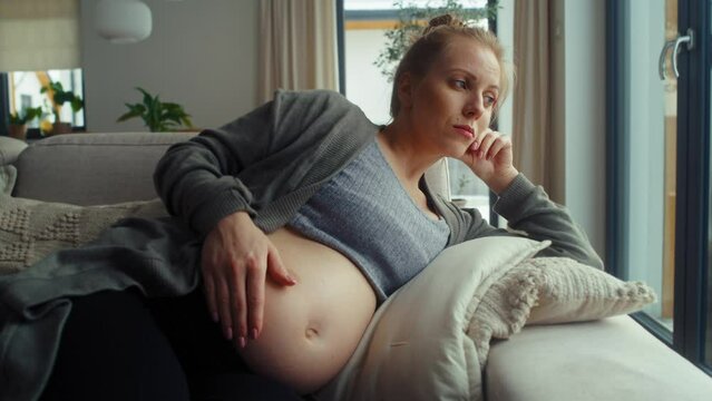 Anxious pregnant woman lying on sofa and touching her abdomen