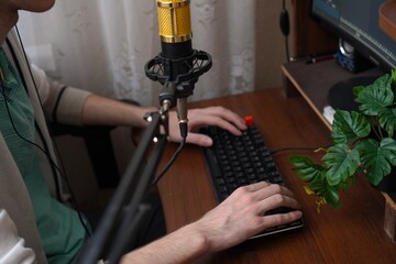 a golden microphone on the background on the hands of a young programmer working on a keyboard on the background of a backlit mouse on a wooden table
