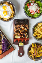 table of barbecue meat served on a table with French fries, salad and grilled vegetables