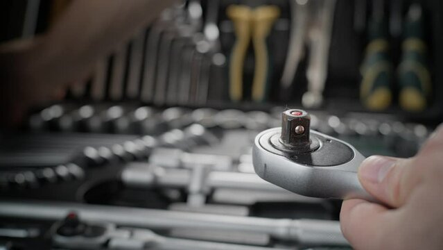 A wrench with a ratchet mechanism with a head for unscrewing nuts is taken out of the set. Shot close-up. Car repair in the garage.