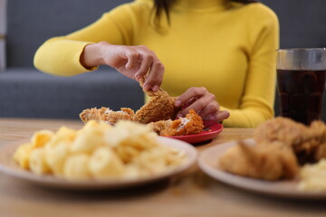 Happy young asian woman eating delicious fried chicken at home. Woman tearing fried chicken meat on a plate.