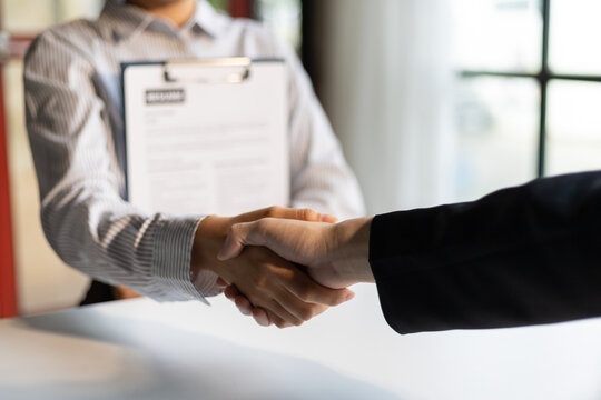 Business, career and placement concept - image of employer sitting in office and shaking hand of young asian woman after successful negotiations or interview.