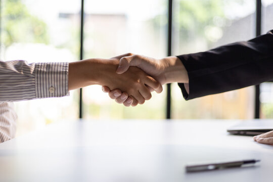 Business, career and placement concept - image of employer sitting in office and shaking hand of young asian woman after successful negotiations or interview.