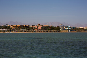 Fototapeta na wymiar Sandy beach of Hurghada overlooking the hotel on the first line of the sea. Relaxing on a sandy beach in summer under the lightning, view from the Red Sea