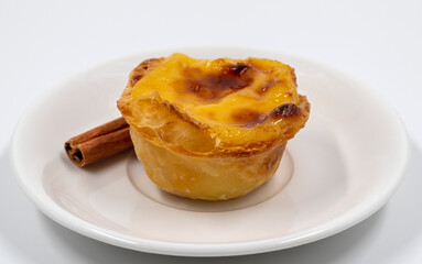 Plate with one Portuguese Pastel de Nata pie with custard and cinnamon sticks. Pastel de Belem is an iconic cup-shaped pastry with a burnt top and a crispy puff pastry crust. Sweet dessert.