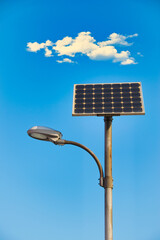 Lamppost powered by solar energy  under a bright blue sky and clouds.