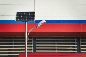 Lamppost powered by solar energy in front of a facade of intense red and blue colors.