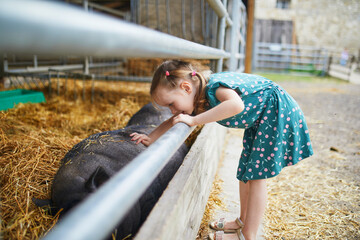 Adorable little girl playing with pig at farm