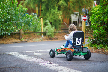 Preschooler girl driving pedal race car in amusement park with road surface marking