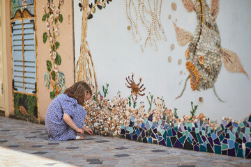 Preschooler girl discovering art decorations made from shells and pebbles on walls in Ile Penotte,...