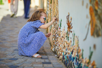 Preschooler girl discovering art decorations made from shells and pebbles on walls in Ile Penotte, Les Sables d'0lonne, Pays de la Loire, France © Ekaterina Pokrovsky