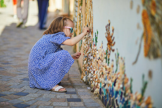 Preschooler girl discovering art decorations made from shells and pebbles on walls in Ile Penotte, Les Sables d'0lonne, Pays de la Loire, France